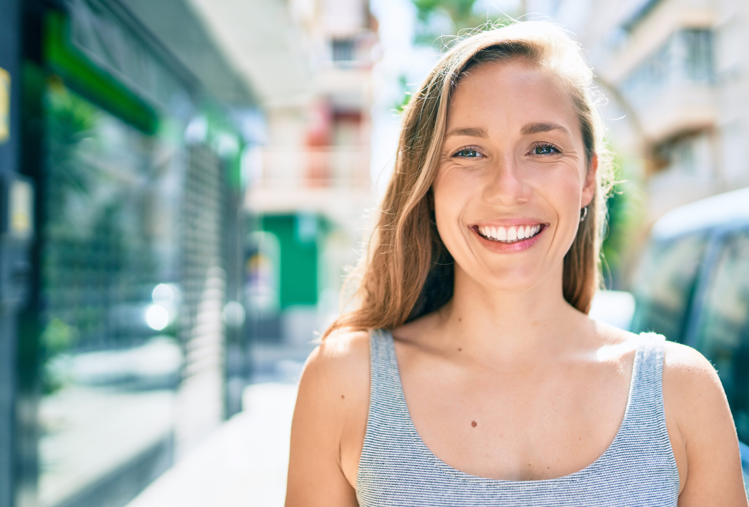closeup of a young blonde woman smiling on city street, perfect white smile
